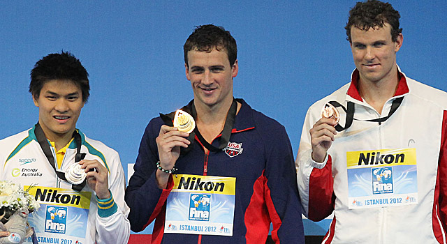 Ryan Lochte (center) poses with his gold after the 100-meter individual medley. (AP)