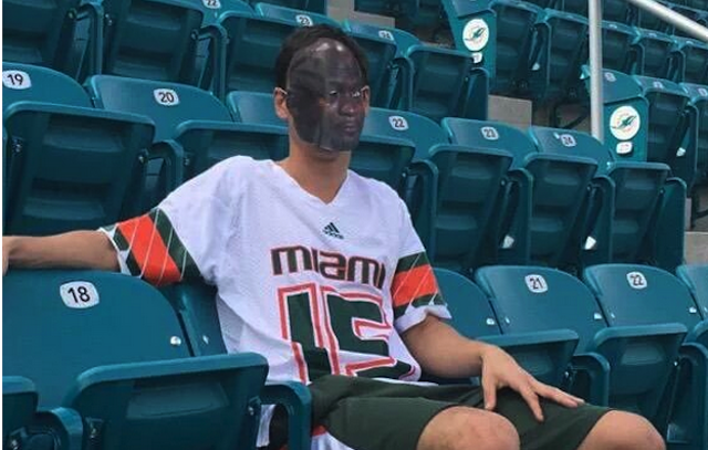 This Miami Hurricanes football fan is sitting in the stands wearing a full  uniform