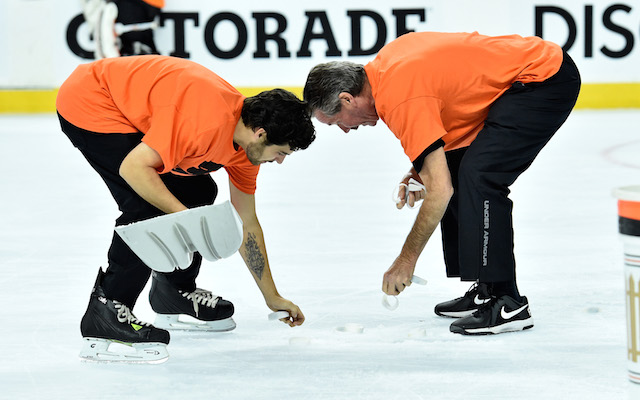Arena workers pick up bracelets that littered the ice in Philadelphia on Monday. (USATSI)